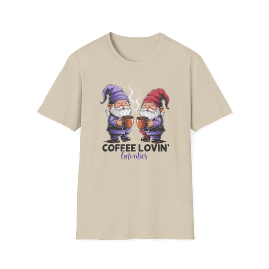 Sand color t-shirt with ’Coffee Lovin’ Gnomies’ text on the bottom of a colorful pair of smiling gnomes standing one in front of the other and holding freshly made coffee on mugs design on a sand color background